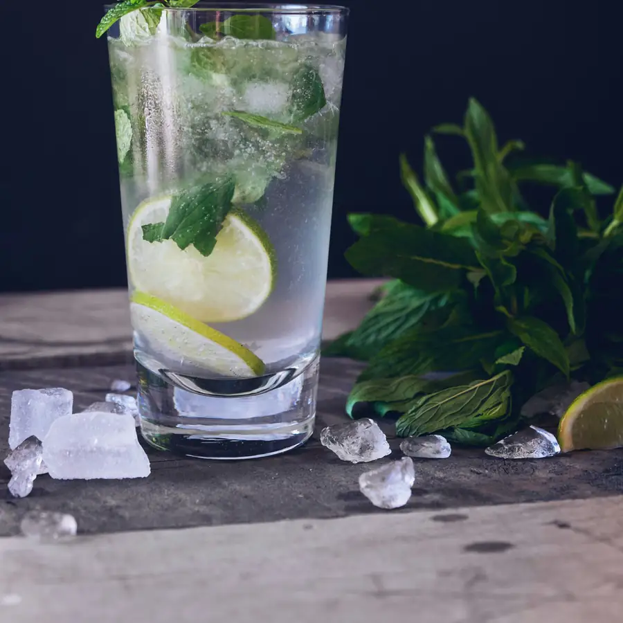Tall glass of sparkling water with ice, lime and mint