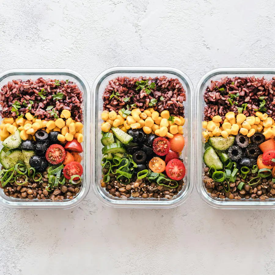 Three lunch boxes of brown rice, chickpeas, olives and salad vegetables
