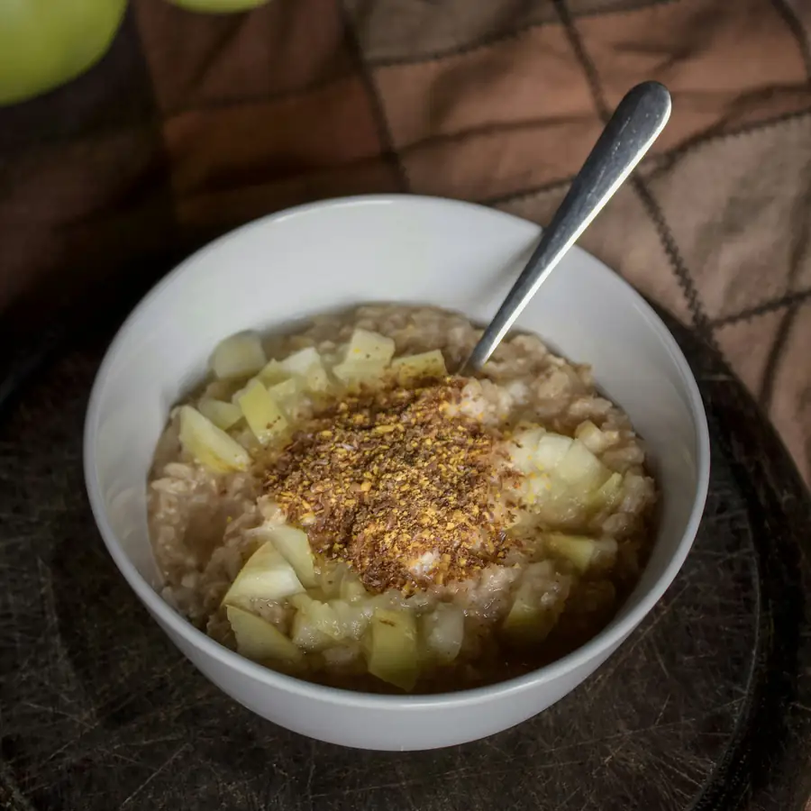 Bowl of oat porridge with chopped apple and a spoon