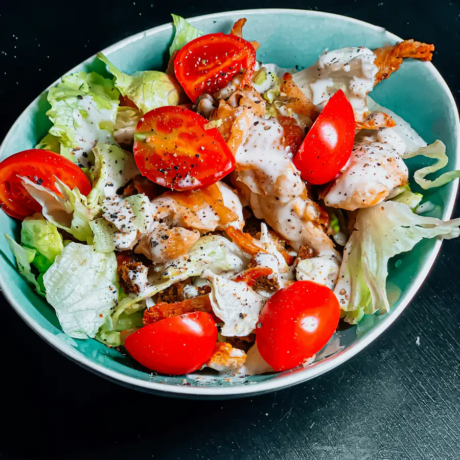 Teal bowl of sliced chicken with lettuce, tomato and radish