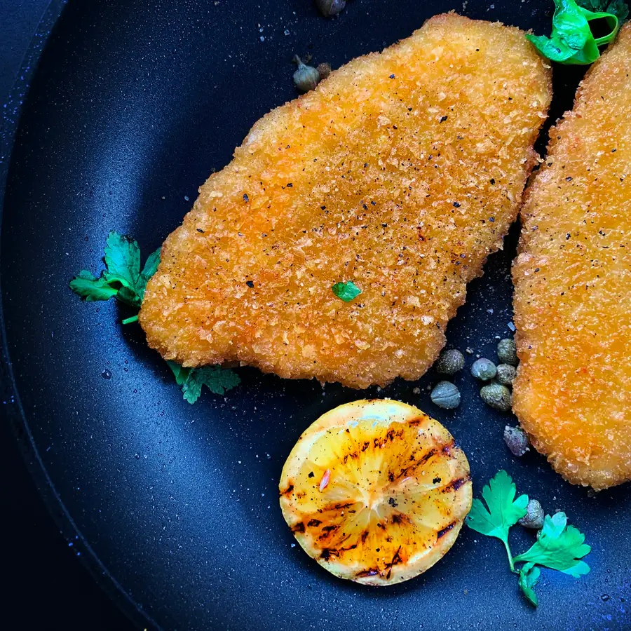 Two crumbed golden fish fillets on a dark plate