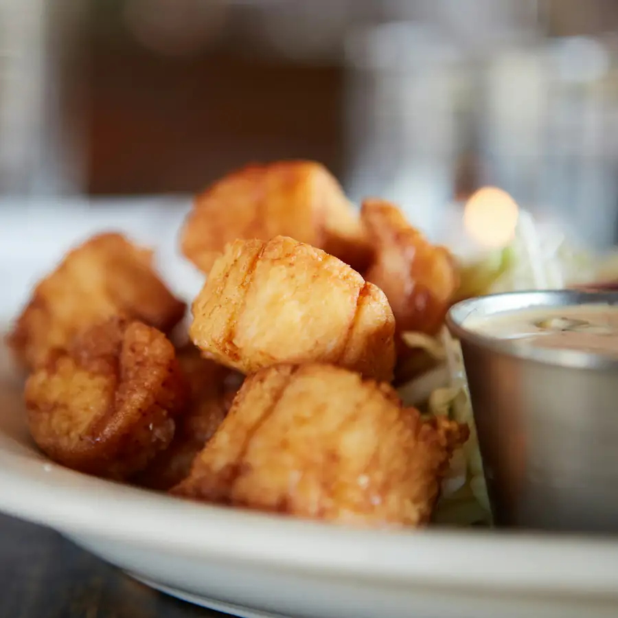 Golden fried pieces on a white plate with a pot of dipping sauce