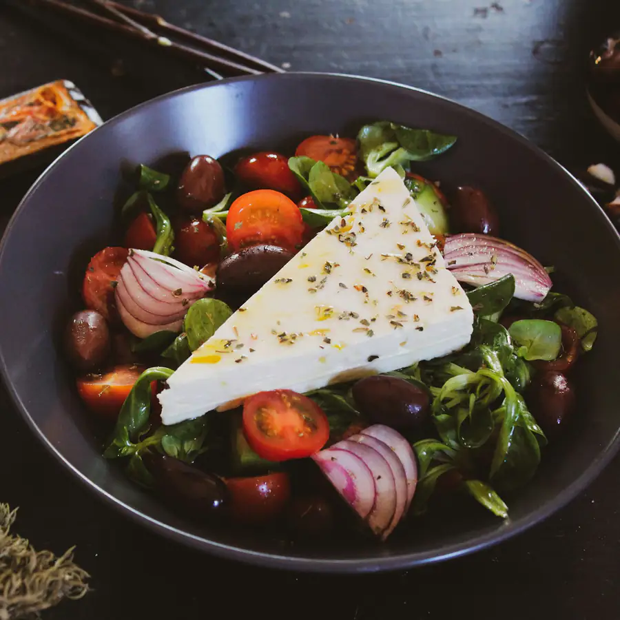 Pan of olives, cherry tomatoes, red onion and spinach with a block of white cheese