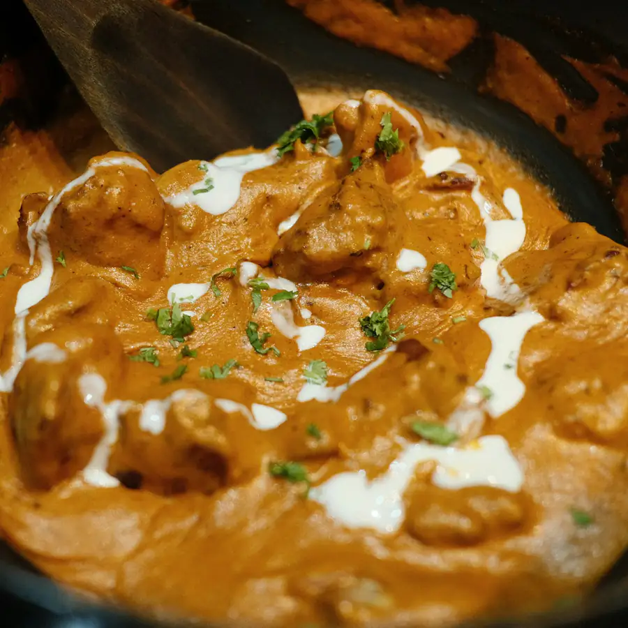 Pan of creamy orange tikka masala with a white swirl and coriander