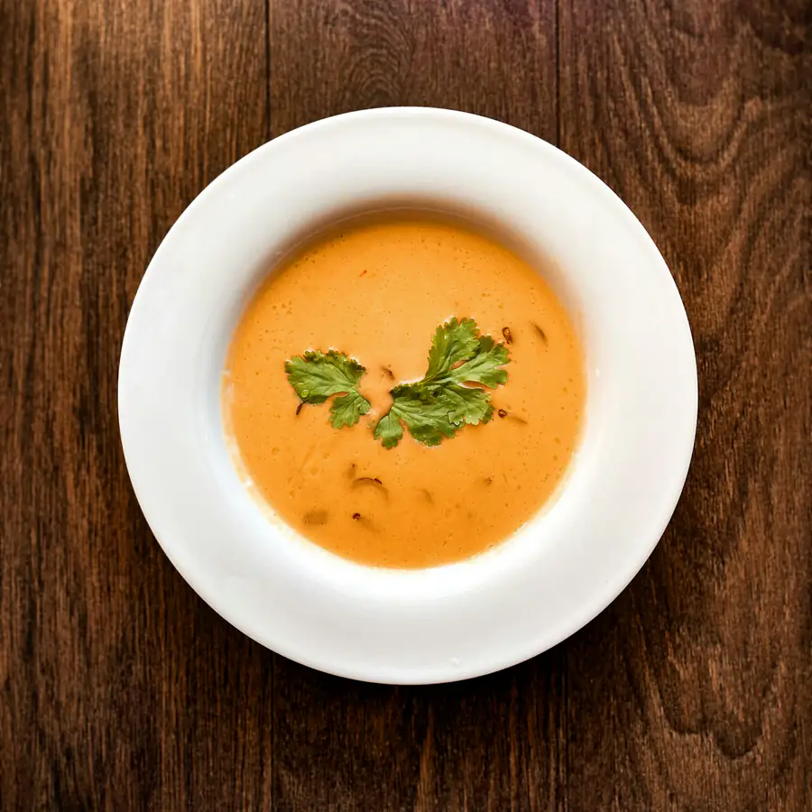 Bowl of smooth carrot and lentil soup with herbs