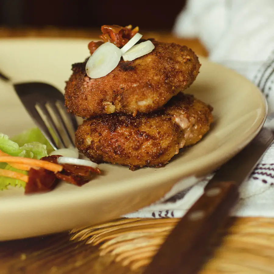 Two golden crumbed fishcakes on a plate with a small salad