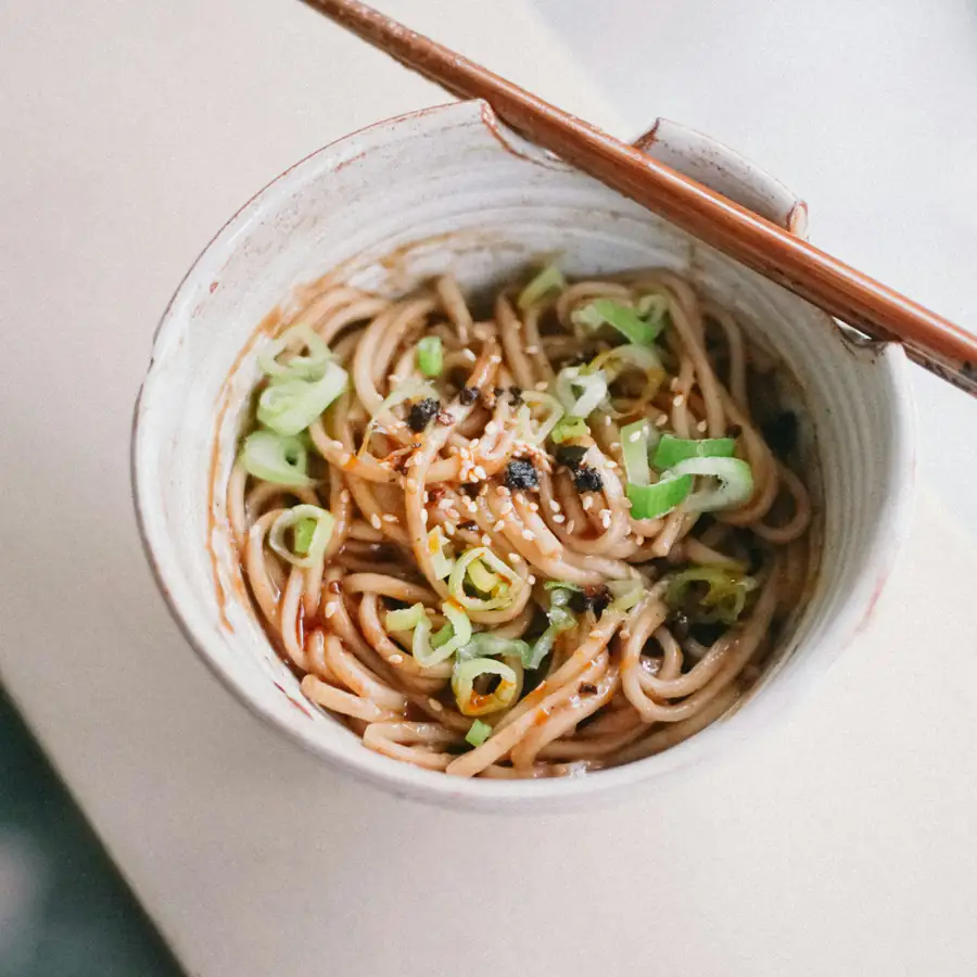Bowl of noodles in a nutty sauce with cucumber and spring onion