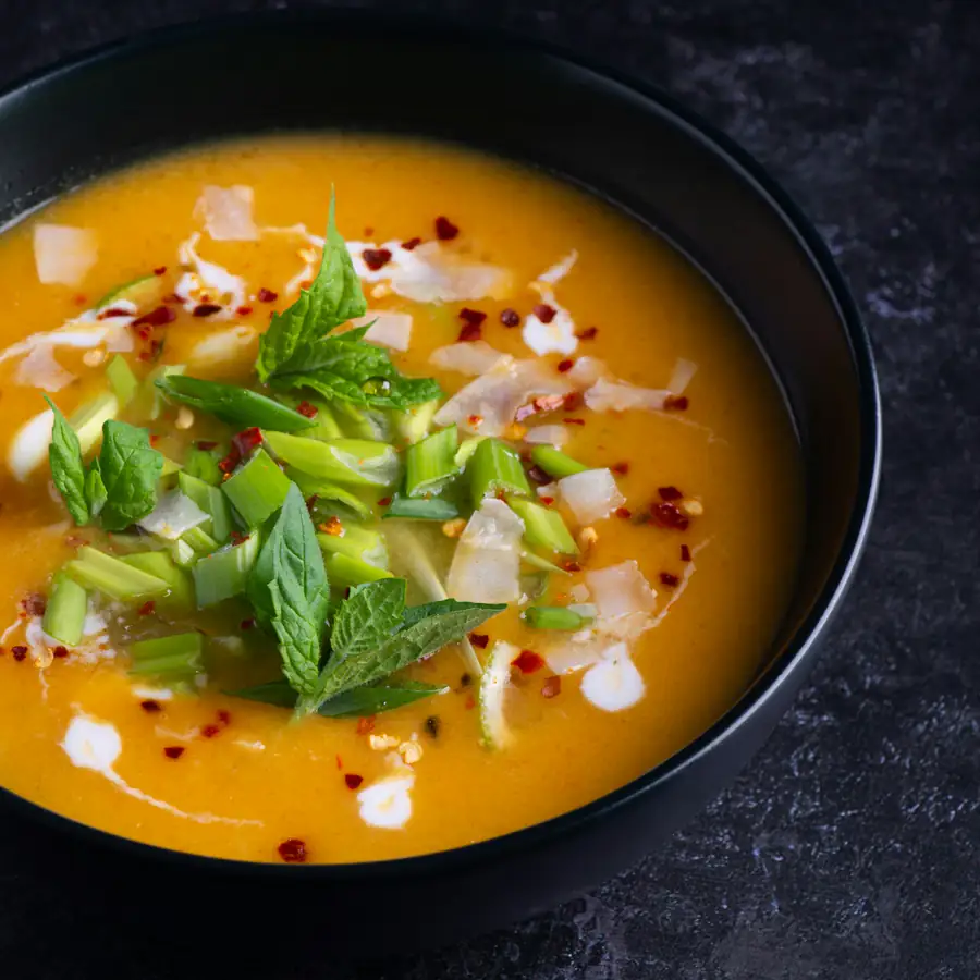 Dark bowl of golden orange soup topped with herbs