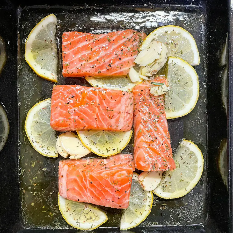 Salmon pieces on a baking tray with lemon slices and garlic