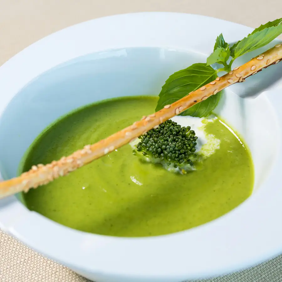 Bowl of green broccoli soup with a breadstick