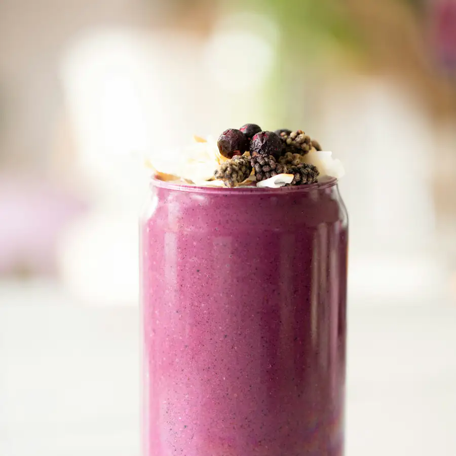 Tall glass of purple berry smoothie topped with berries