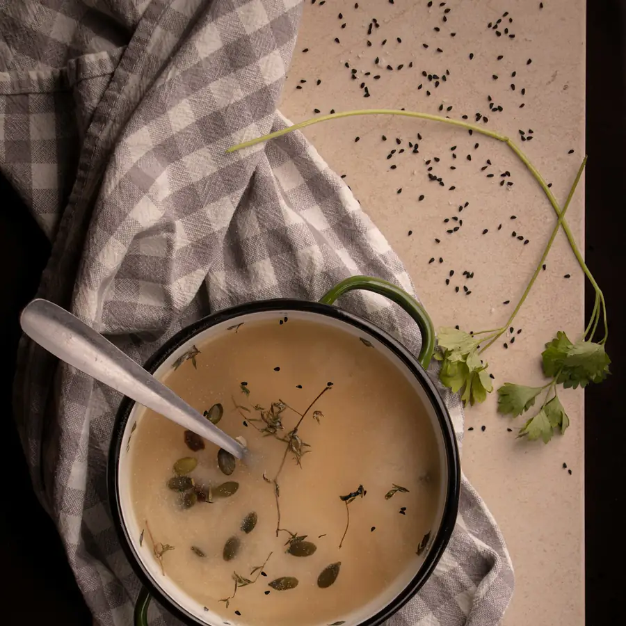 Pot of pale creamy vegetable soup with seeds and herbs