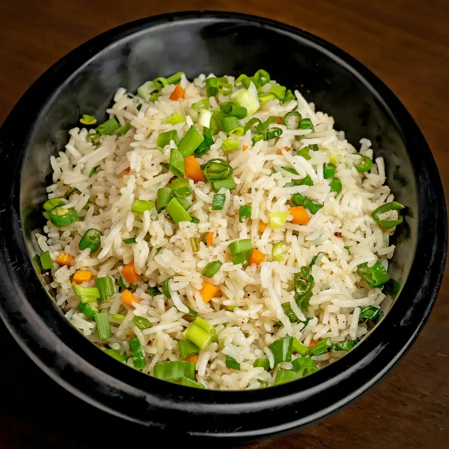 Bowl of fried rice with peas, carrots and spring onion