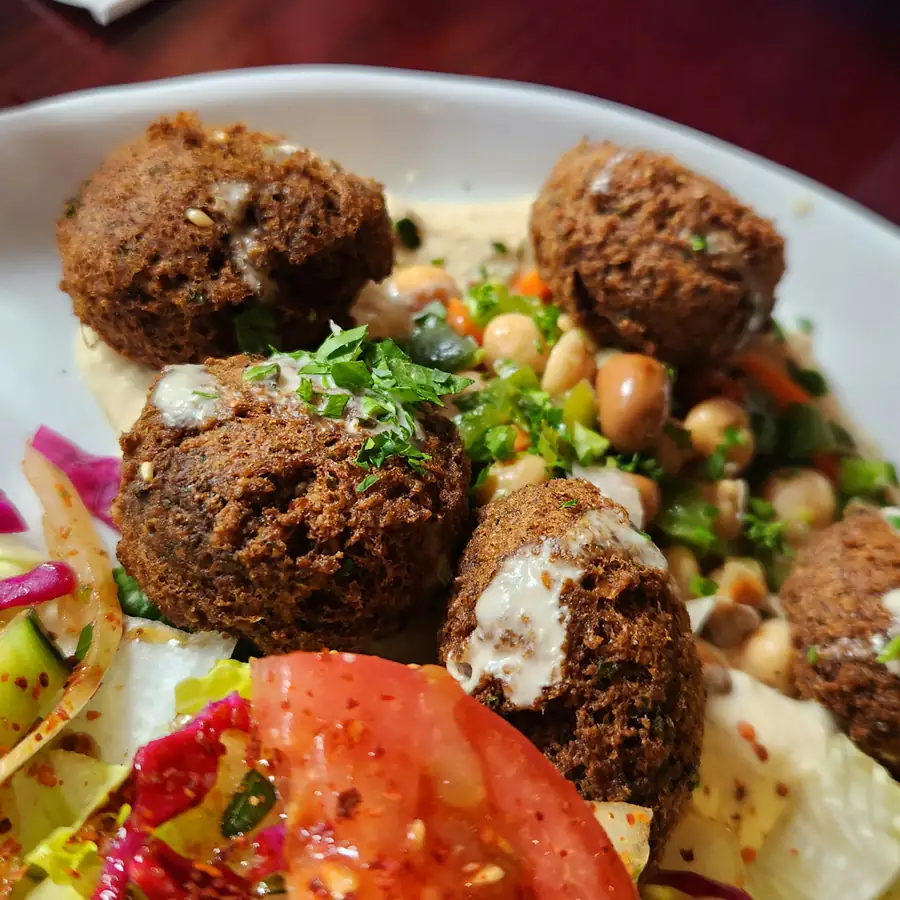 Four falafel on a plate with hummus, chickpeas and chopped parsley