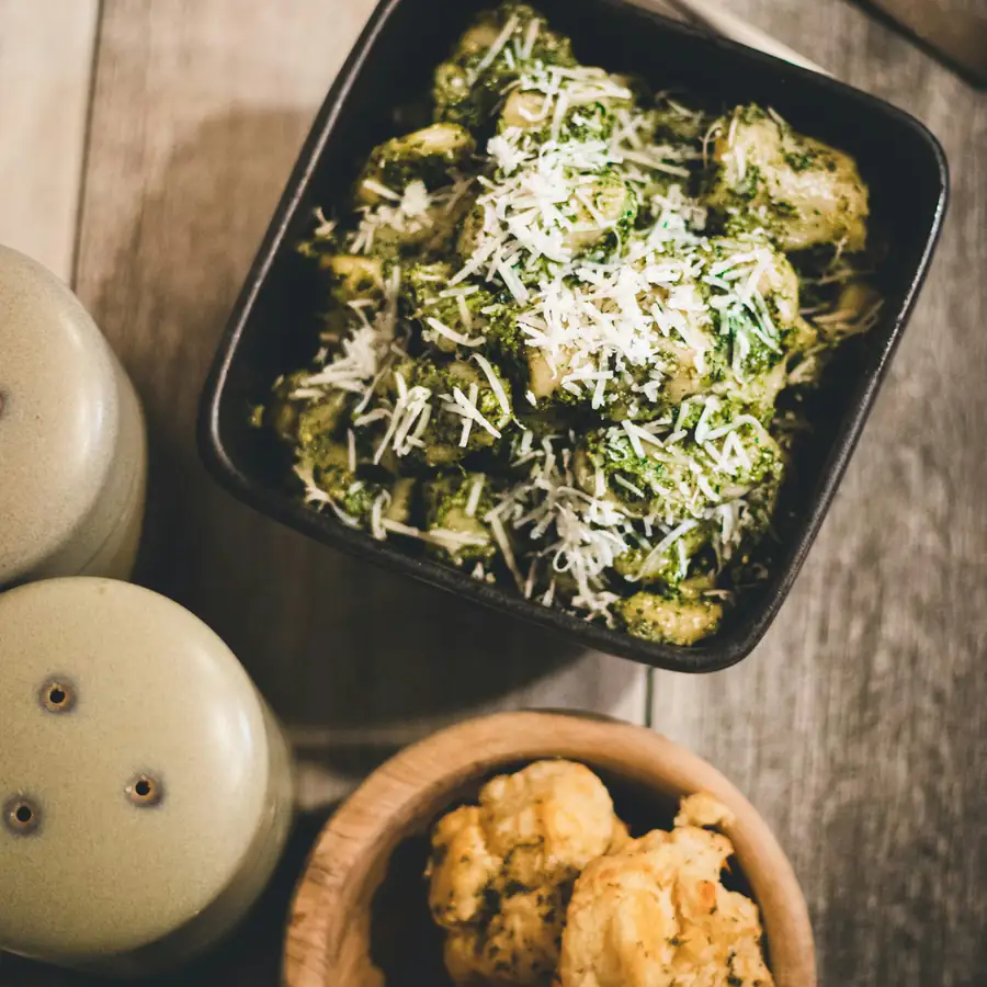 Black bowl of gnocchi with shredded greens and grated cheese