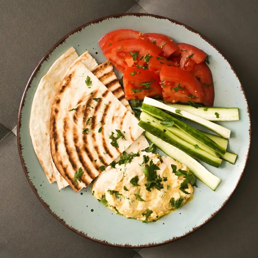Plate of hummus with flatbread, roast carrot and cucumber