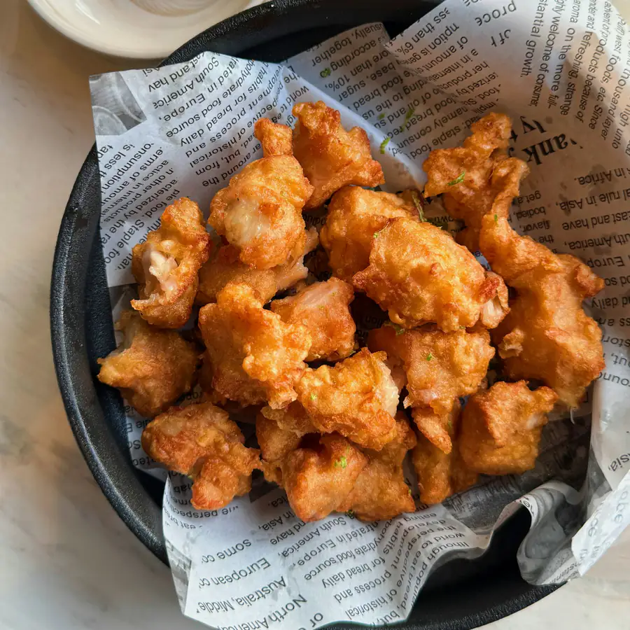 Basket of crispy salt and pepper chicken pieces on newspaper