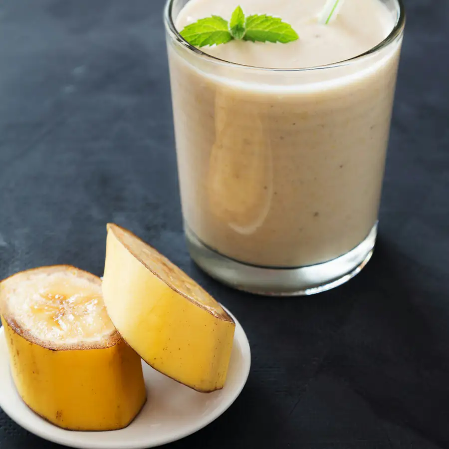 Tall glass of creamy smoothie with mint leaves and a halved citrus fruit