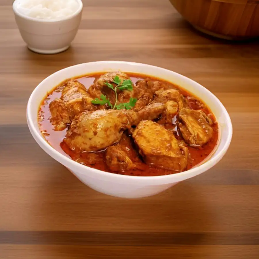 Bowl of chicken curry in a rich sauce beside a bowl of rice