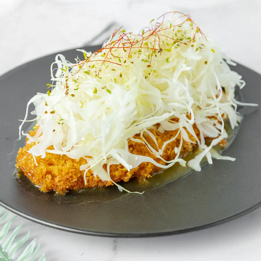 Breaded chicken katsu with shredded cabbage and carrot on a metal plate