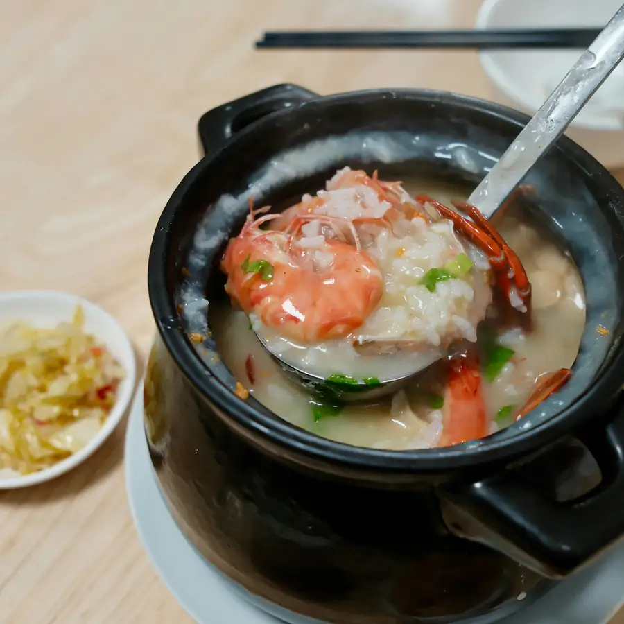 Black pot of rice congee with a spoon lifting prawn and shredded chicken