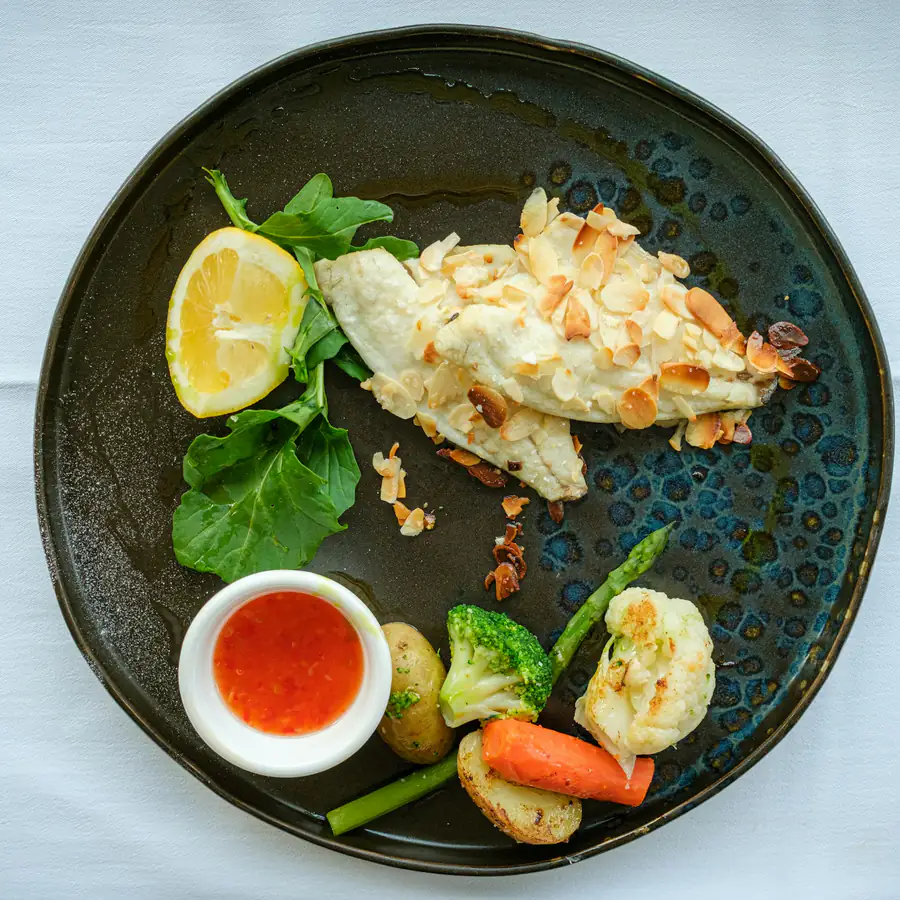 White fish fillet with lemon and roast vegetables on a dark plate
