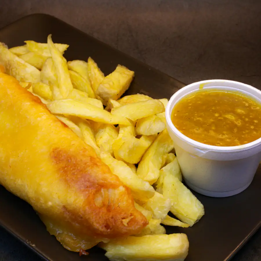Bowl of battered fish and chips with a pot of sauce
