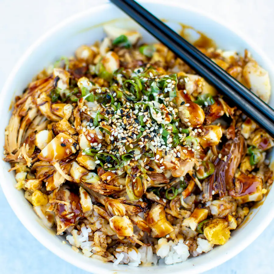 Bowl of rice topped with a sauced filling, corn, cucumber and sesame seeds